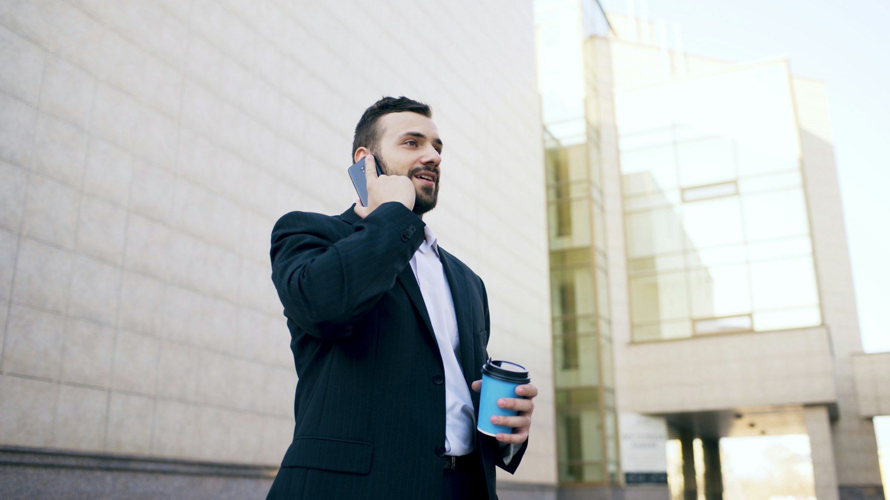 Professional on a phone call outside an office building, holding a coffee